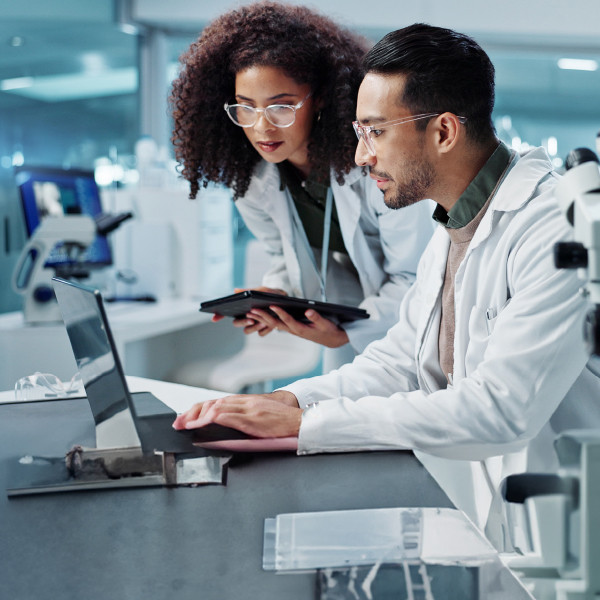 Zwei Labortechniker, die in einem biowissenschaftlichen Labor auf einen Laptop-Bildschirm schauen 